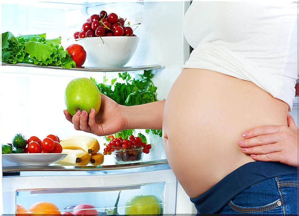 Pregnant woman opening the fridge and picking up an apple